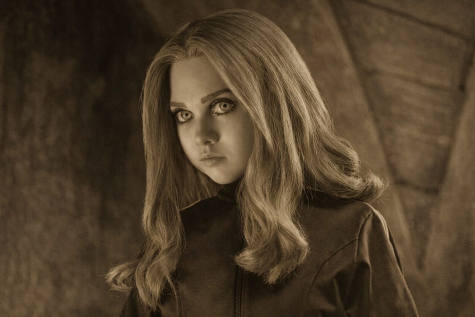 薄暗い背景の前で、金髪の少女が真剣な目つきで見つめるアップ写真