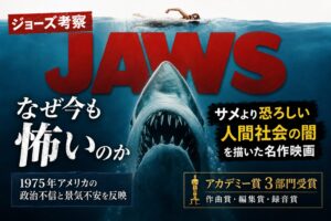 映画『ジョーズ』の考察記事用アイキャッチ。海面を泳ぐ人物の下に巨大ザメが迫り、サメより恐ろしい人間社会の闇とアカデミー賞3部門受賞を伝えるデザイン。